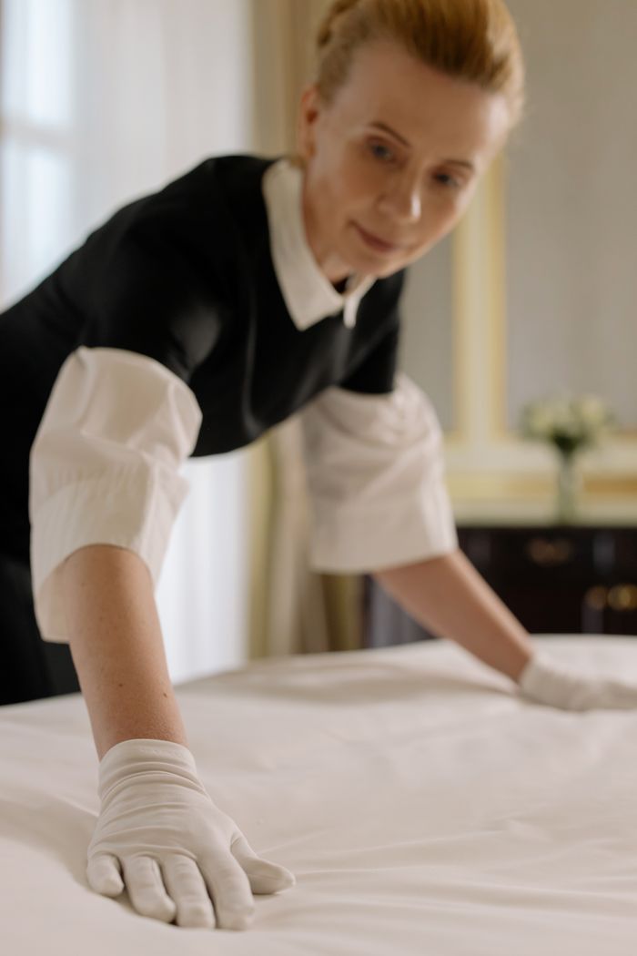 mobile-01 A housekeeper gracefully arranges bed sheets in a luxurious hotel room, demonstrating hospitality expertise.