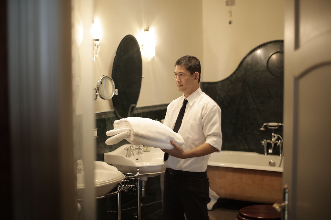 brand-01 Side view of young male employee holding stack of white towels while standing in bathroom of luxury hotel