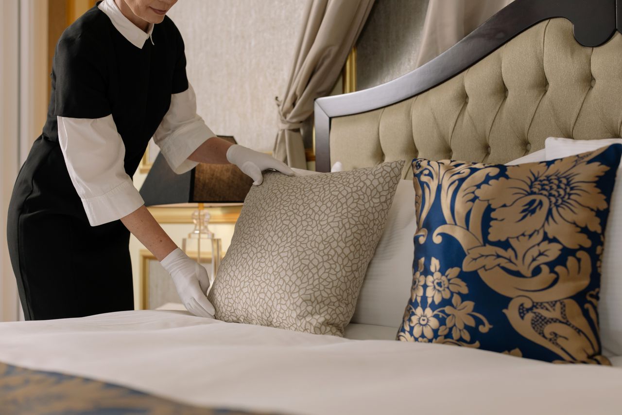 A chambermaid arranges pillows in a luxurious hotel room, highlighting comfort and elegance.